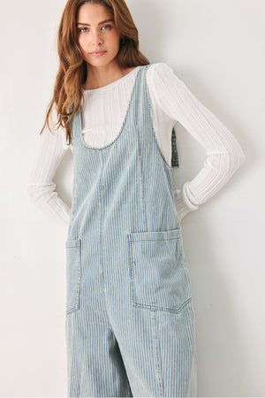 A woman wearing a light blue and white vertically striped corduroy bib jumpsuit over a white long-sleeve top | FREEMARKET