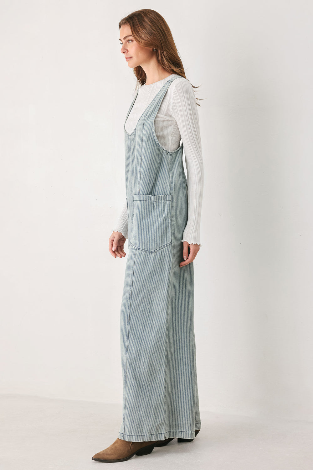A woman wearing a light blue and white vertically striped corduroy bib jumpsuit over a white long-sleeve top | FREEMARKET
