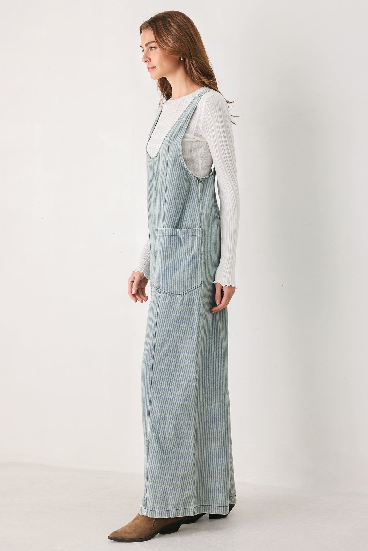 A woman wearing a light blue and white vertically striped corduroy bib jumpsuit over a white long-sleeve top | FREEMARKET
