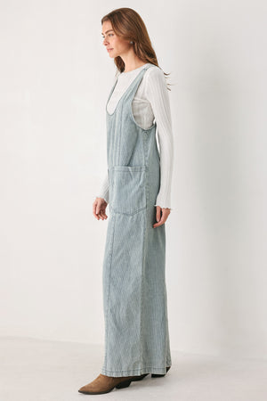 A woman wearing a light blue and white vertically striped corduroy bib jumpsuit over a white long-sleeve top | FREEMARKET