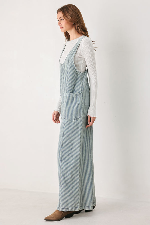 A woman wearing a light blue and white vertically striped corduroy bib jumpsuit over a white long-sleeve top | FREEMARKET