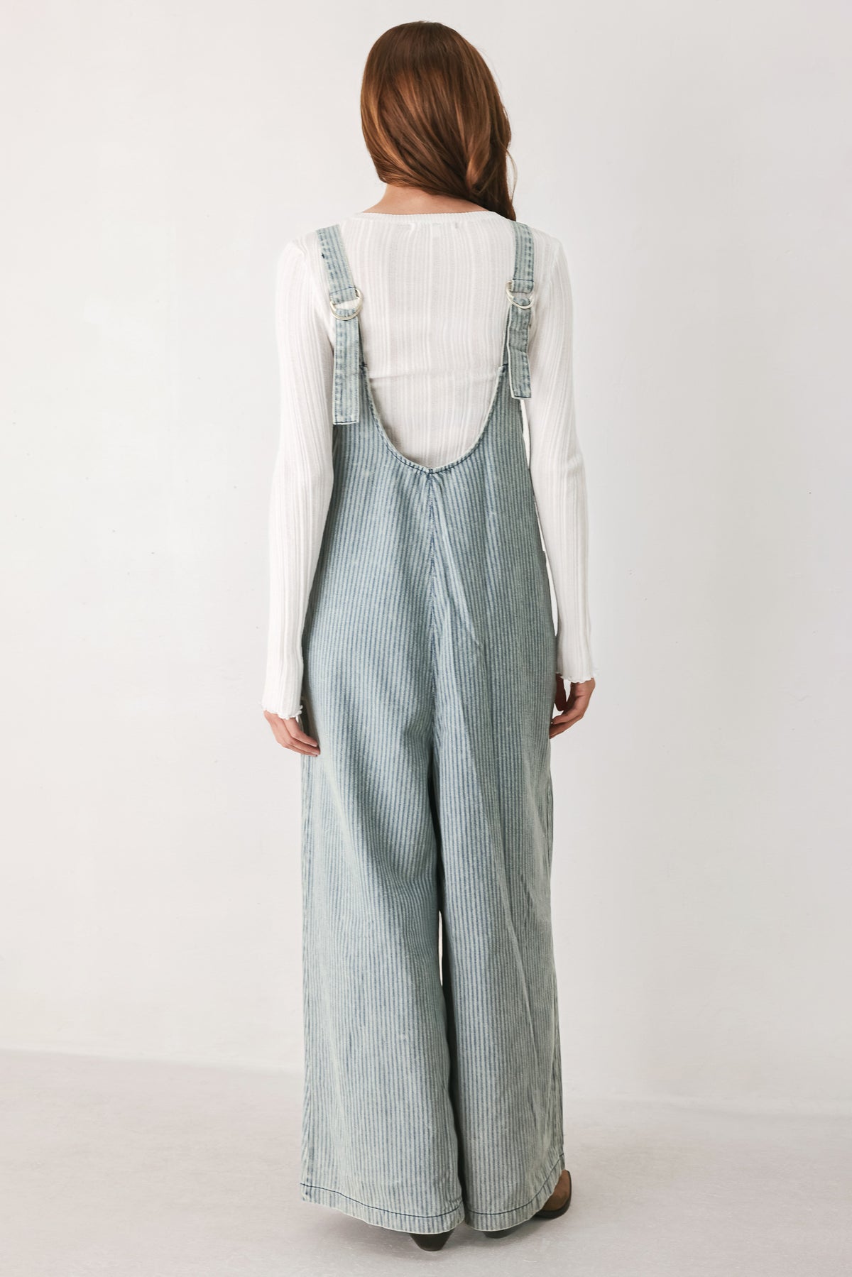 A woman wearing a light blue and white vertically striped corduroy bib jumpsuit over a white long-sleeve top | FREEMARKET