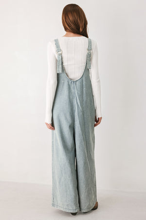 A woman wearing a light blue and white vertically striped corduroy bib jumpsuit over a white long-sleeve top | FREEMARKET