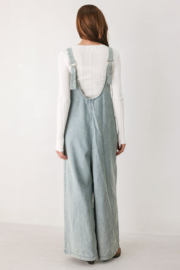 A woman wearing a light blue and white vertically striped corduroy bib jumpsuit over a white long-sleeve top | FREEMARKET