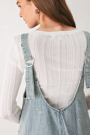 A woman wearing a light blue and white vertically striped corduroy bib jumpsuit over a white long-sleeve top | FREEMARKET