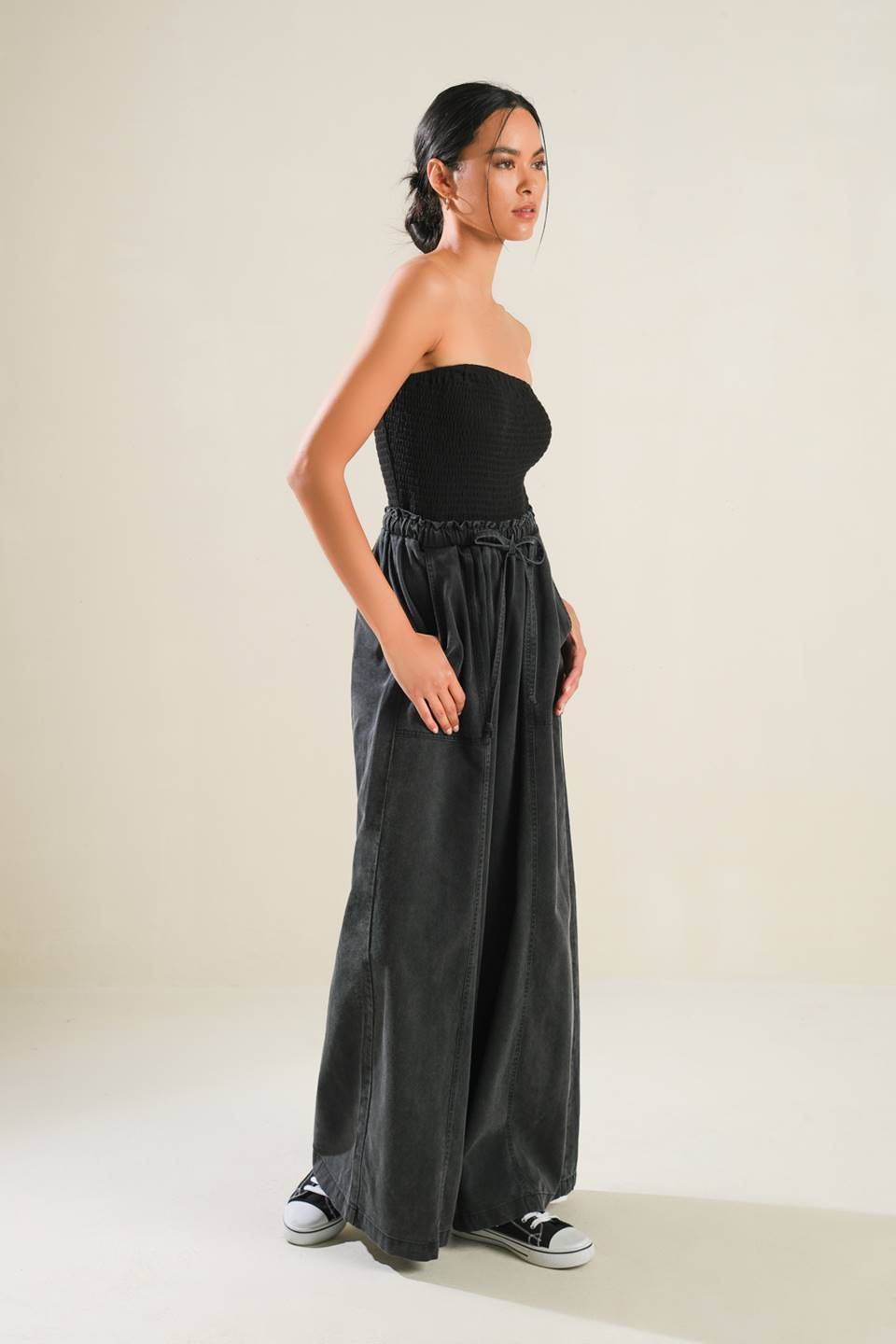 A mix media jumpsuit featuring strapless smocked tube top, contrasting pant with elasticized waist and tie, side pockets and wide leg