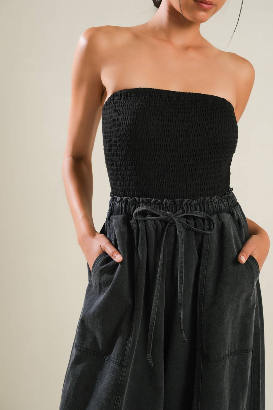 A mix media jumpsuit featuring strapless smocked tube top, contrasting pant with elasticized waist and tie, side pockets and wide leg