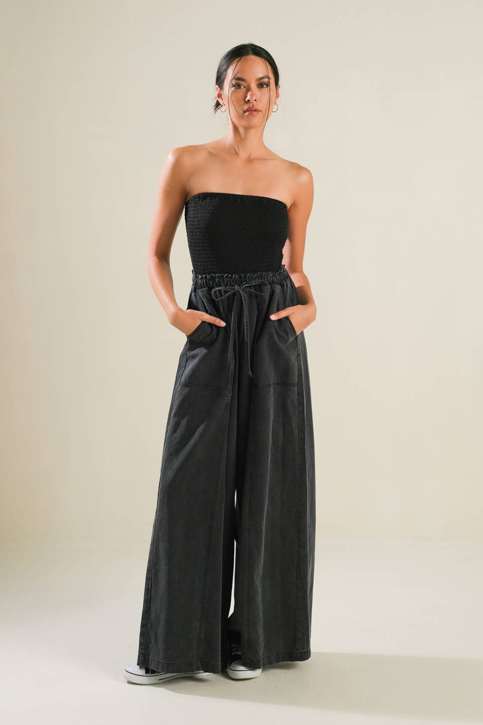 A mix media jumpsuit featuring strapless smocked tube top, contrasting pant with elasticized waist and tie, side pockets and wide leg