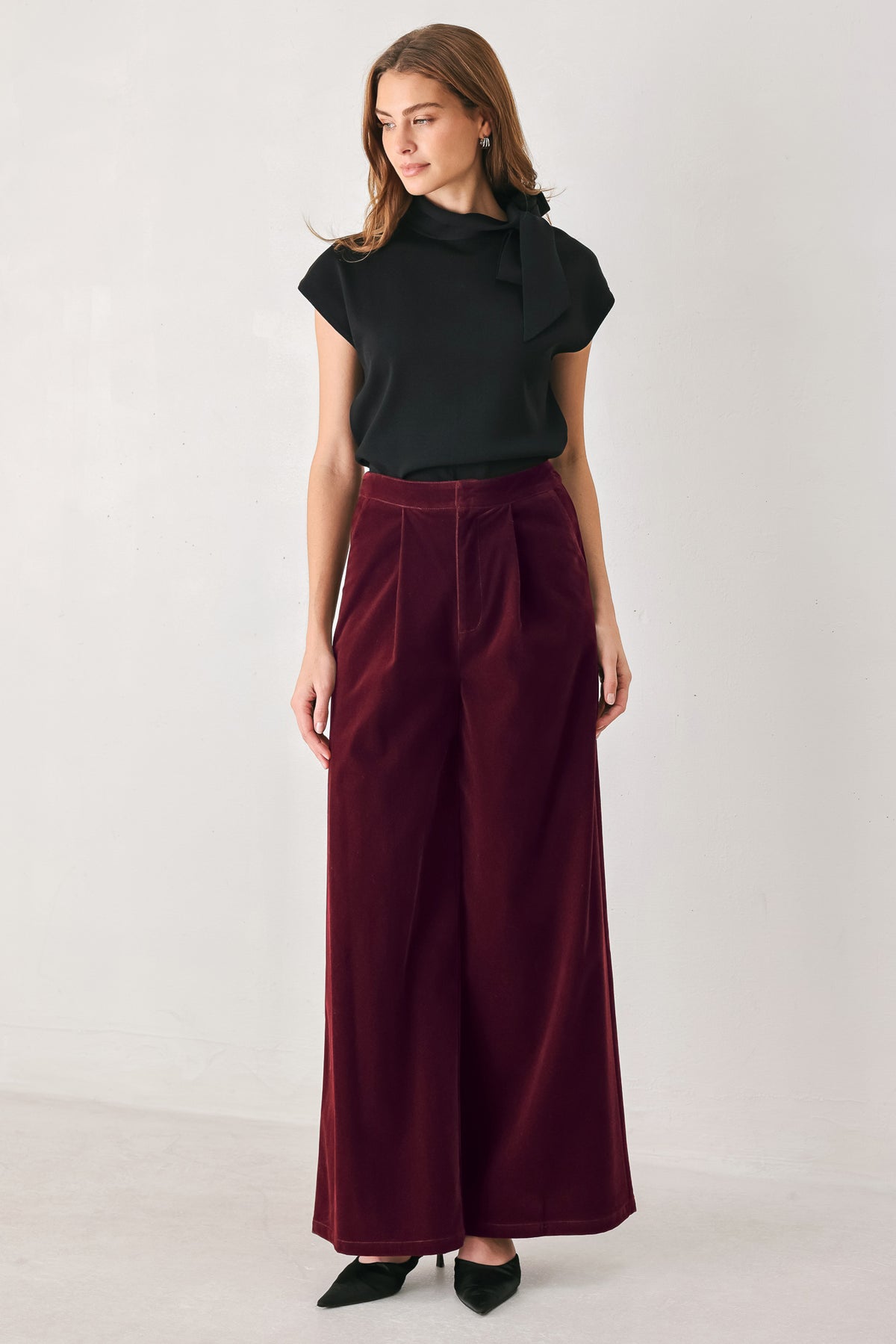 A person wearing high-waisted, wide-leg burgundy velvet pants with black pointed-toe heels | FREEMARKET