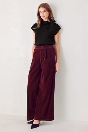 A person wearing high-waisted, wide-leg burgundy velvet pants with black pointed-toe heels | FREEMARKET
