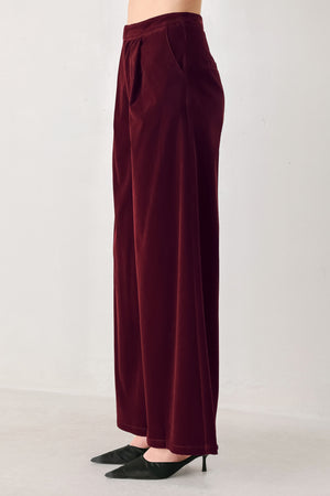 A person wearing high-waisted, wide-leg burgundy velvet pants with black pointed-toe heels | FREEMARKET