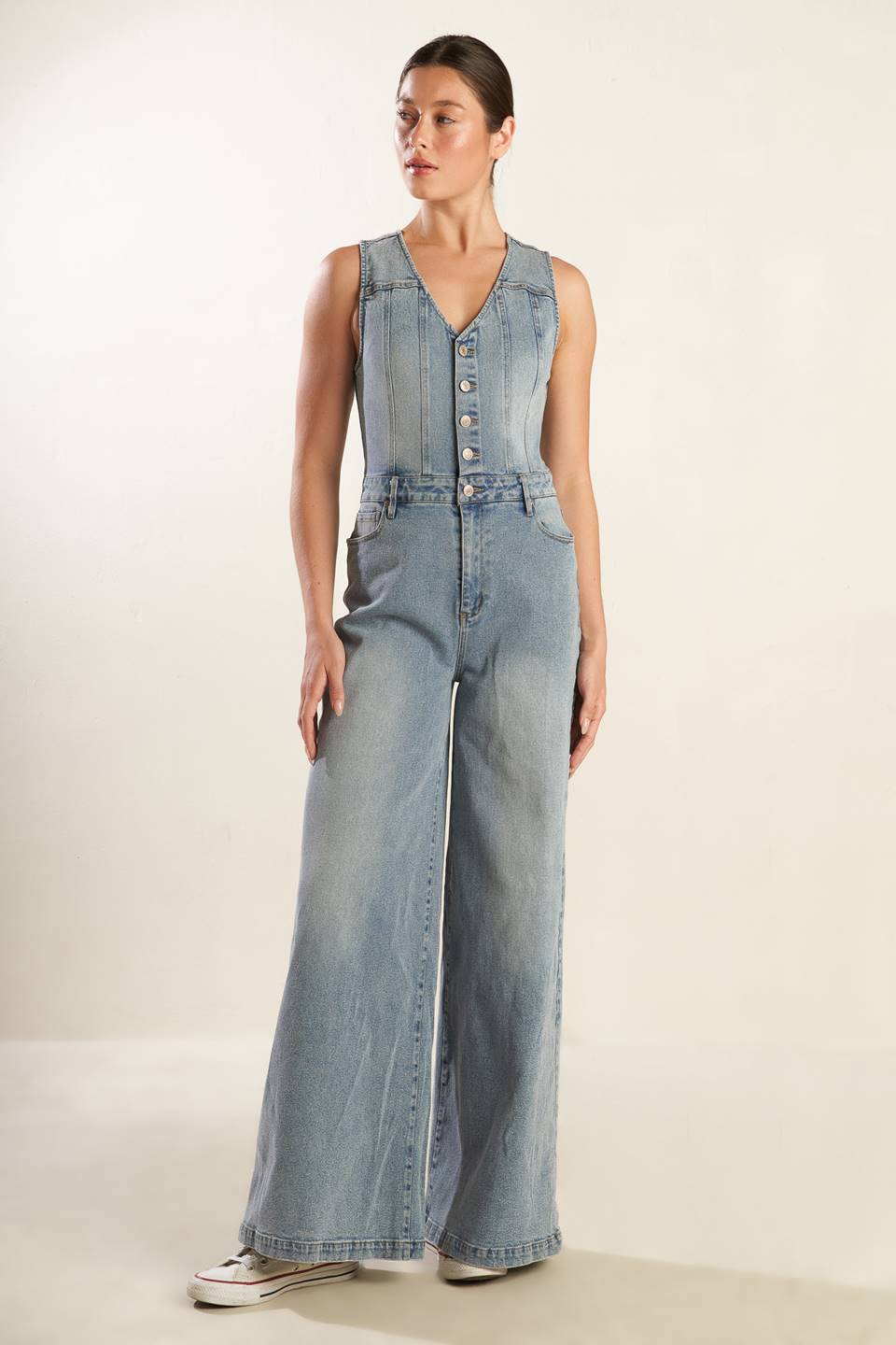 A washed light denim jumpsuit featuring V neckline, sleeveless, button down bodice, front zipper closure, side and back pockets and wide leg.