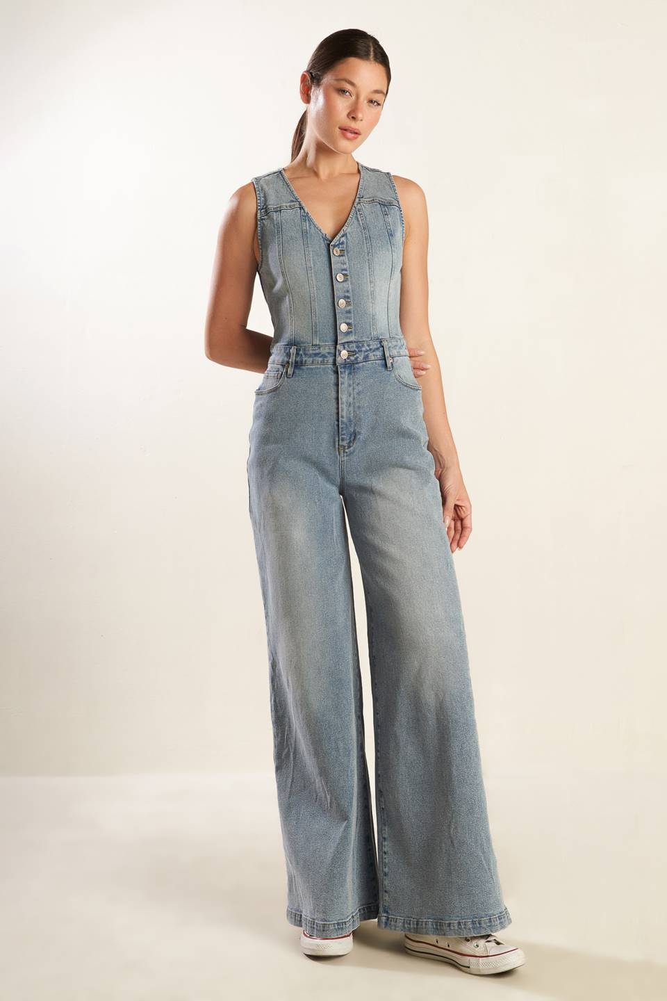 A washed light denim jumpsuit featuring V neckline, sleeveless, button down bodice, front zipper closure, side and back pockets and wide leg.