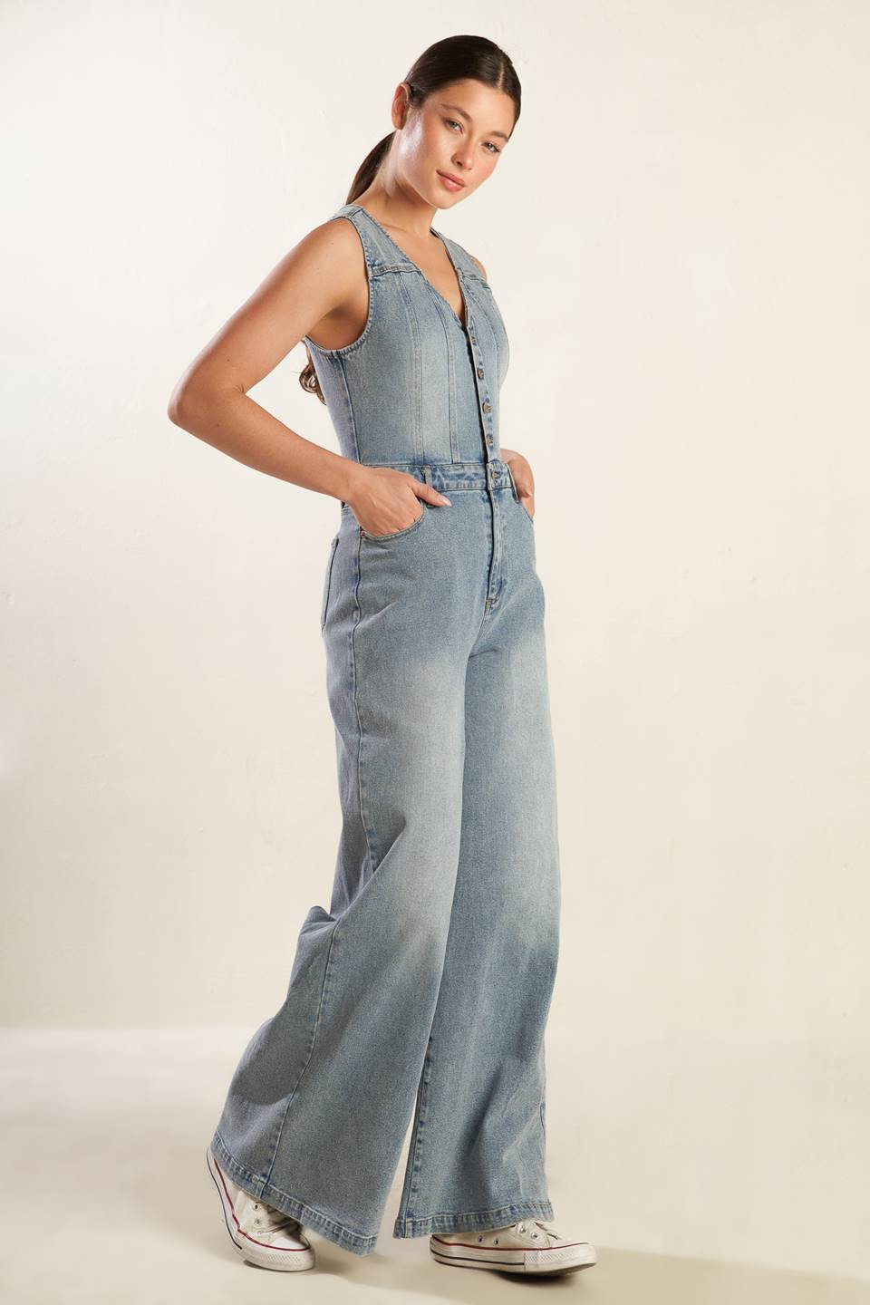 A washed light denim jumpsuit featuring V neckline, sleeveless, button down bodice, front zipper closure, side and back pockets and wide leg.