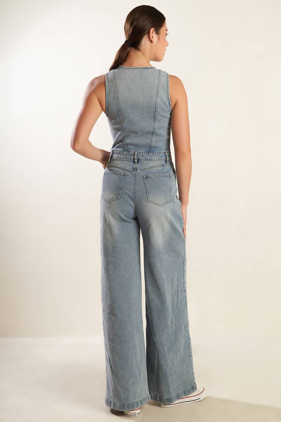 A washed light denim jumpsuit featuring V neckline, sleeveless, button down bodice, front zipper closure, side and back pockets and wide leg.