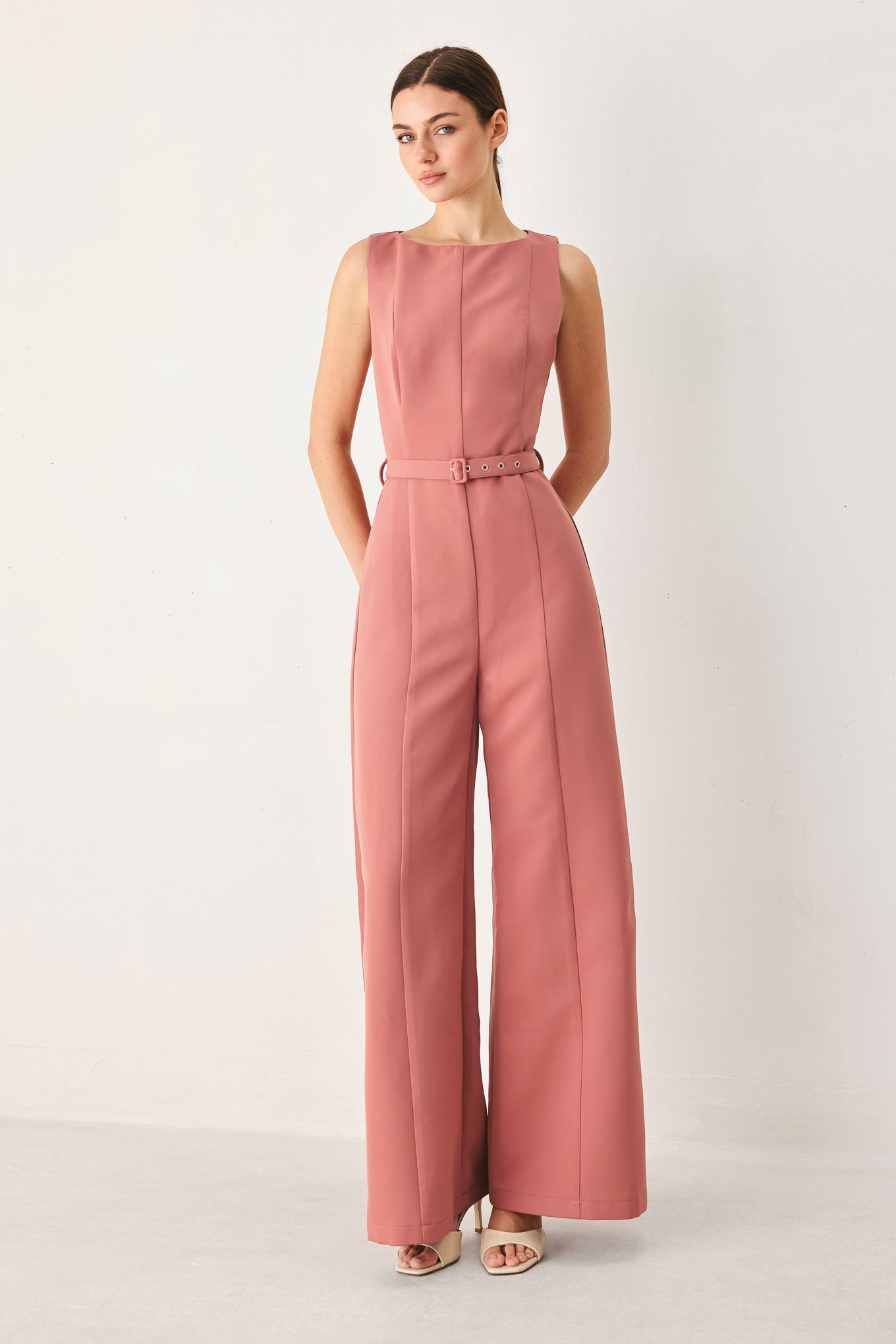 Woman wearing a sleeveless pink rose jumpsuit featuring wide neckline, self belt, wide leg and back zipper closure | FREEMARKET