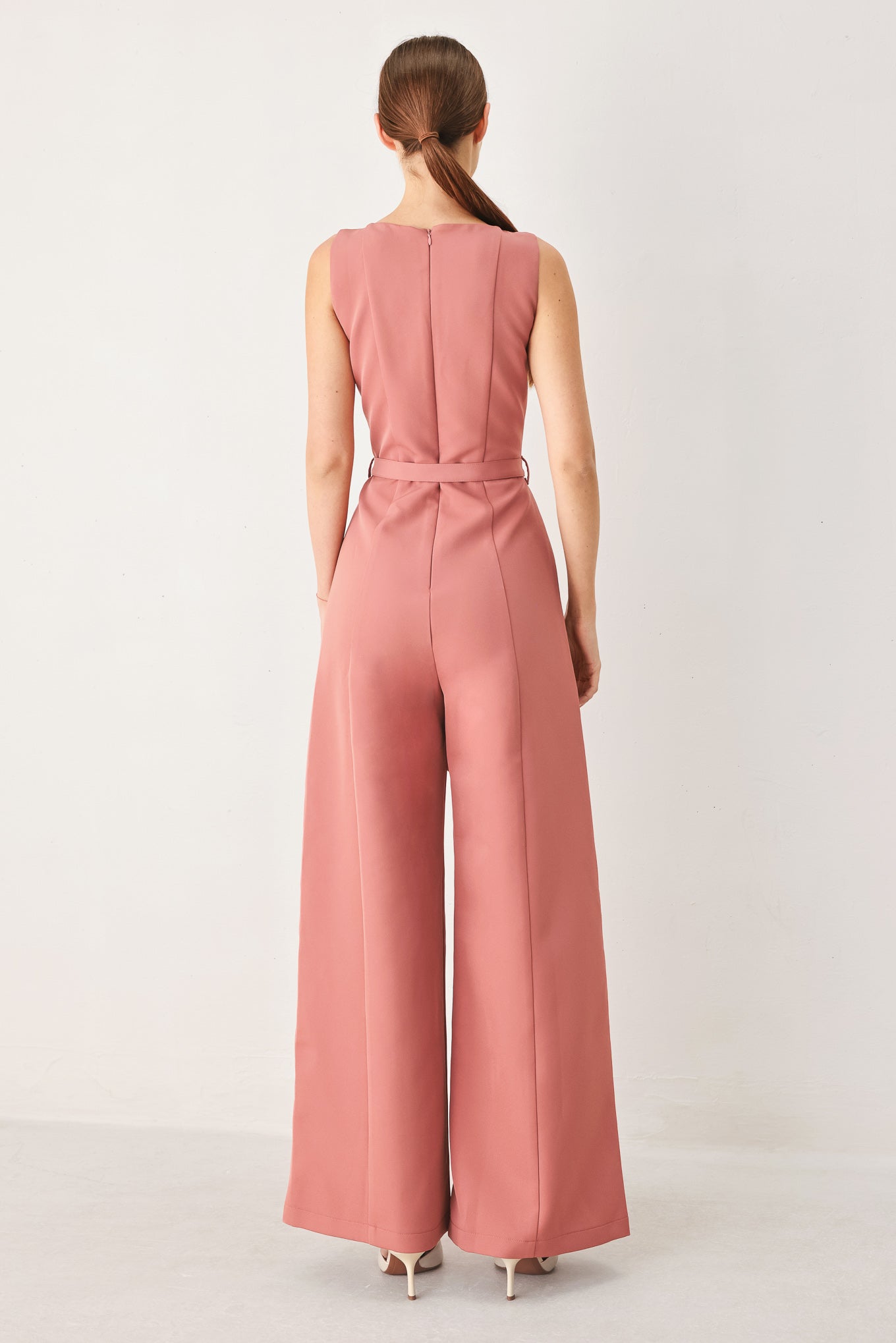 Woman wearing a sleeveless pink rose jumpsuit featuring wide neckline, self belt, wide leg and back zipper closure | FREEMARKET