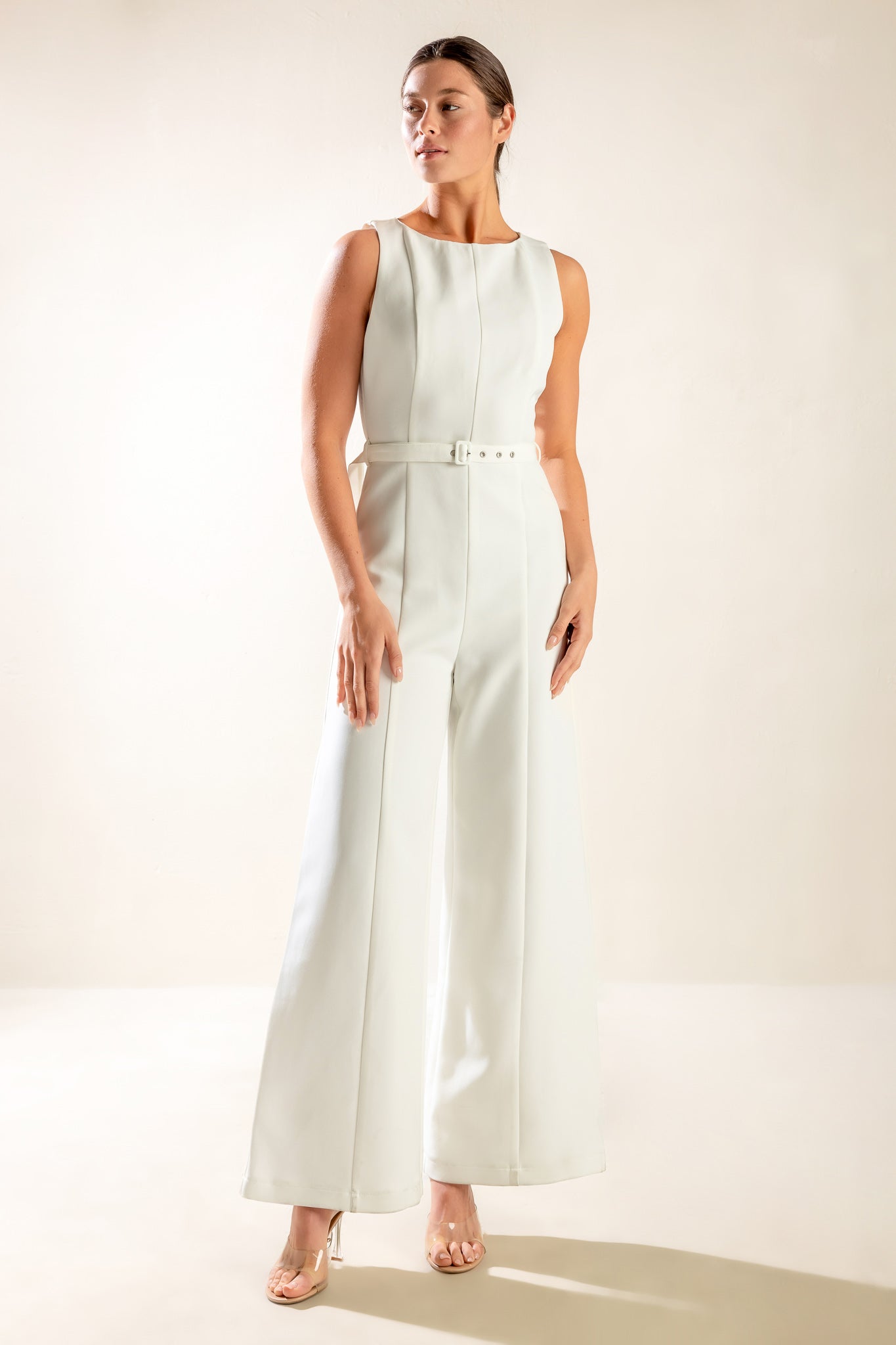 Woman wearing a sleeveless white jumpsuit featuring wide neckline, self belt, wide leg and back zipper closure | FREEMARKET