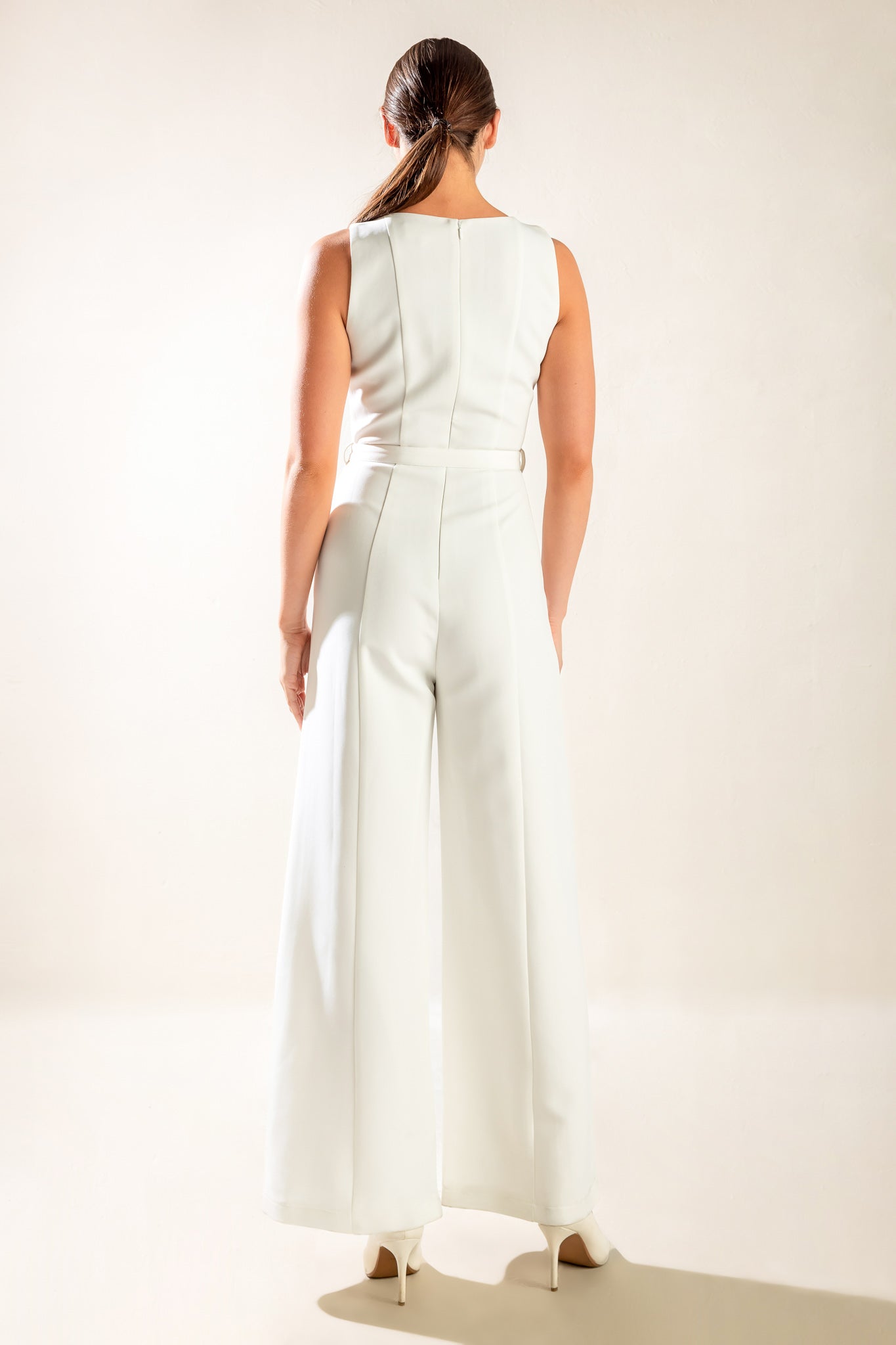 Woman wearing a sleeveless white jumpsuit featuring wide neckline, self belt, wide leg and back zipper closure | FREEMARKET