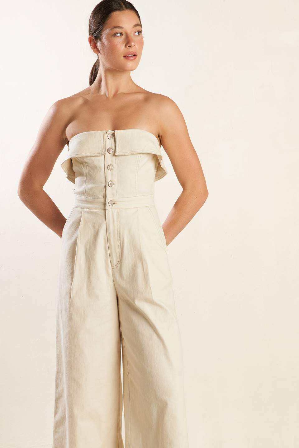 A strapless solid woven jumpsuit featuring front button down and zipper closure, side pockets and wide leg.