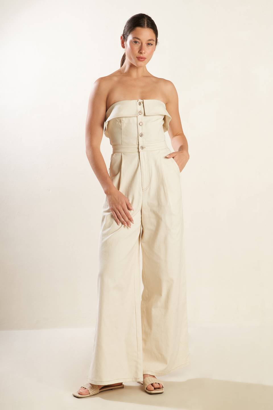 A strapless solid woven jumpsuit featuring front button down and zipper closure, side pockets and wide leg.