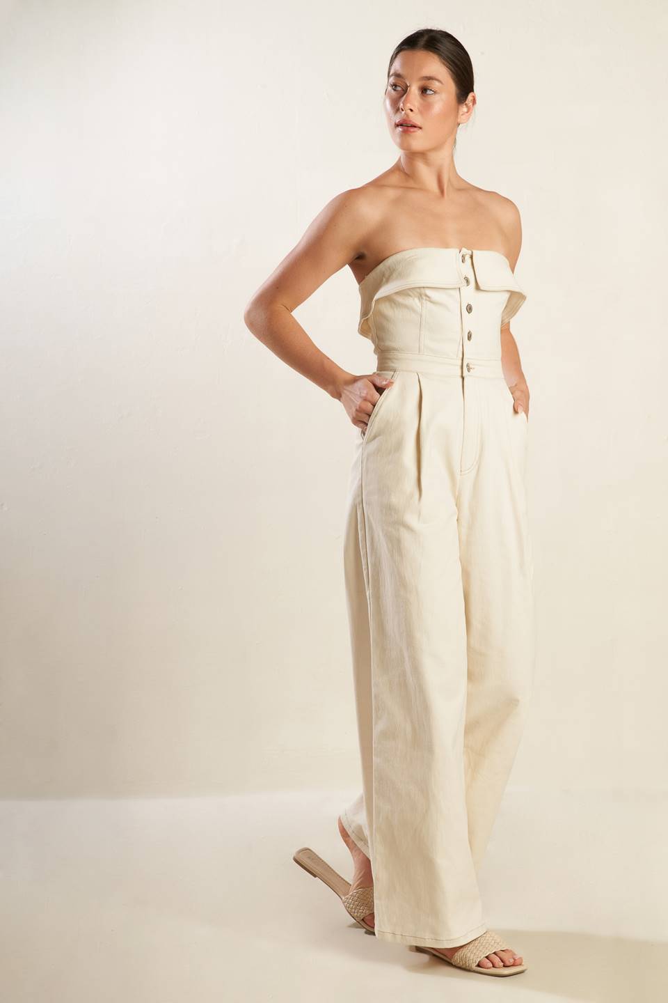 A strapless solid woven jumpsuit featuring front button down and zipper closure, side pockets and wide leg.