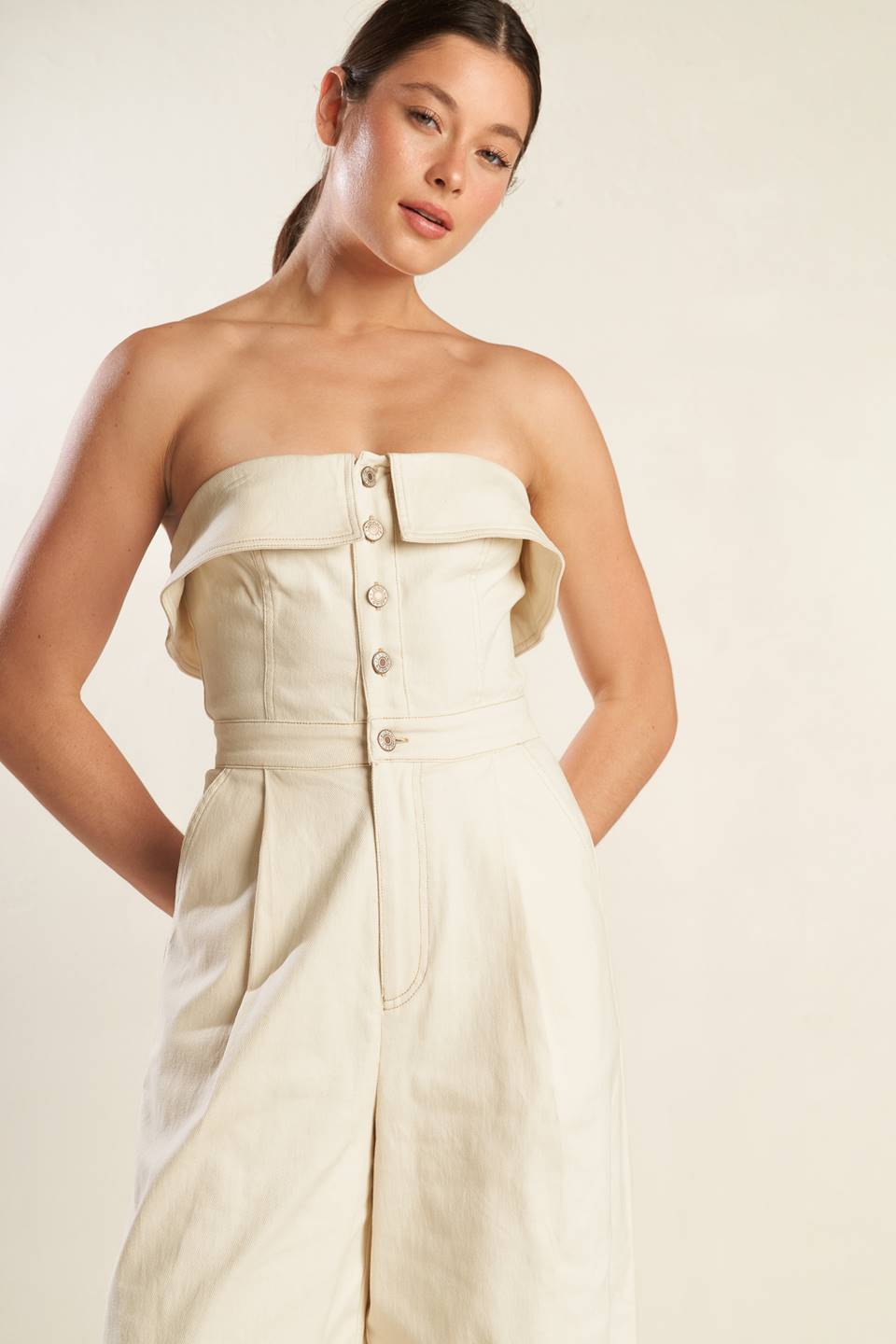 A strapless solid woven jumpsuit featuring front button down and zipper closure, side pockets and wide leg.