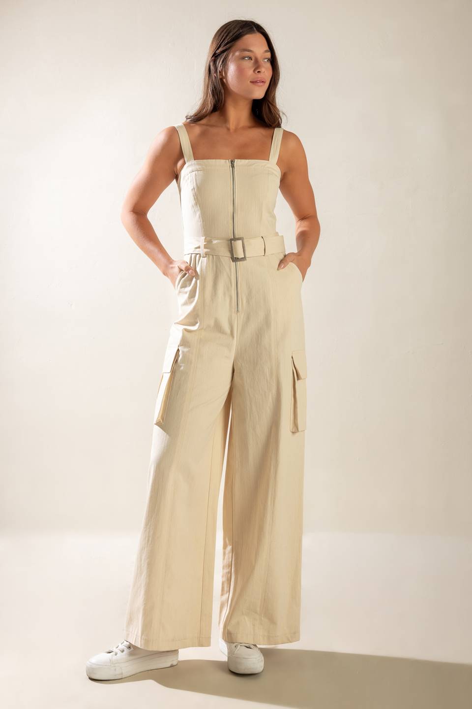 A solid woven jumpsuit featuring straight neckline, straps, front zipper closure, self belt and side/cargo pockets.