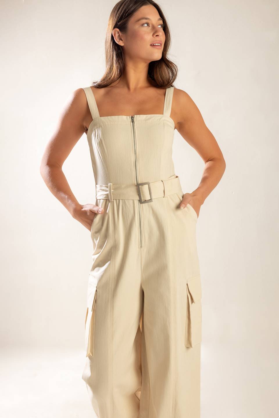 A solid woven jumpsuit featuring straight neckline, straps, front zipper closure, self belt and side/cargo pockets.