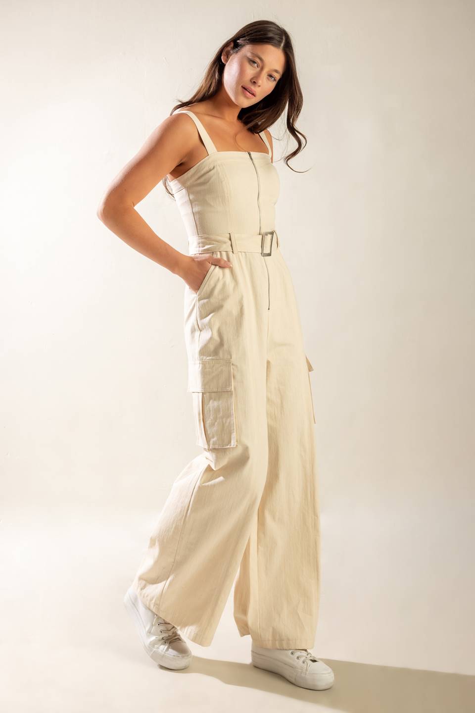 A solid woven jumpsuit featuring straight neckline, straps, front zipper closure, self belt and side/cargo pockets.