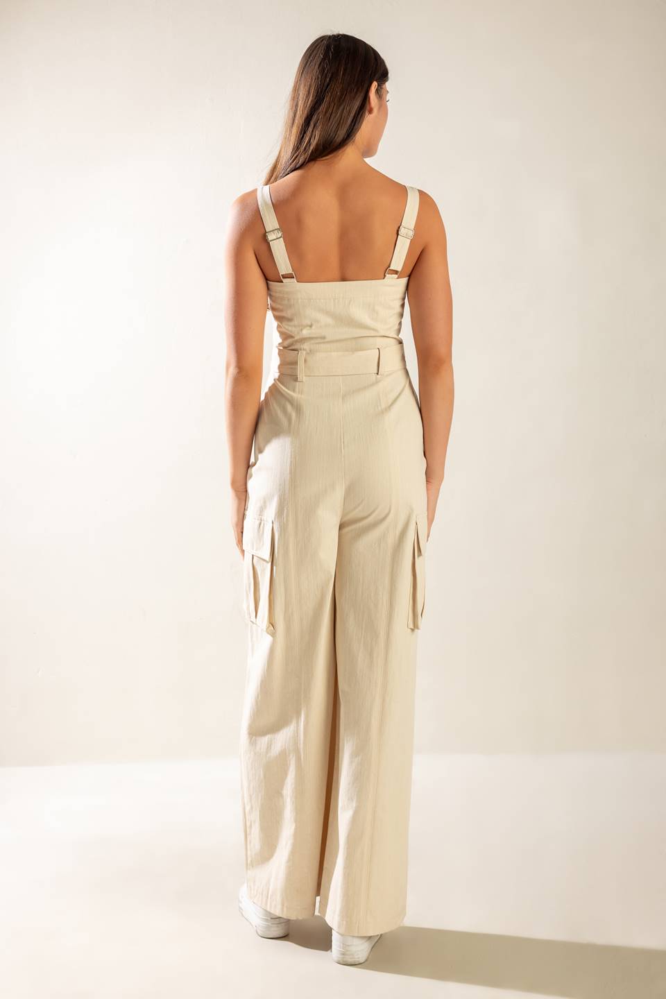 A solid woven jumpsuit featuring straight neckline, straps, front zipper closure, self belt and side/cargo pockets.