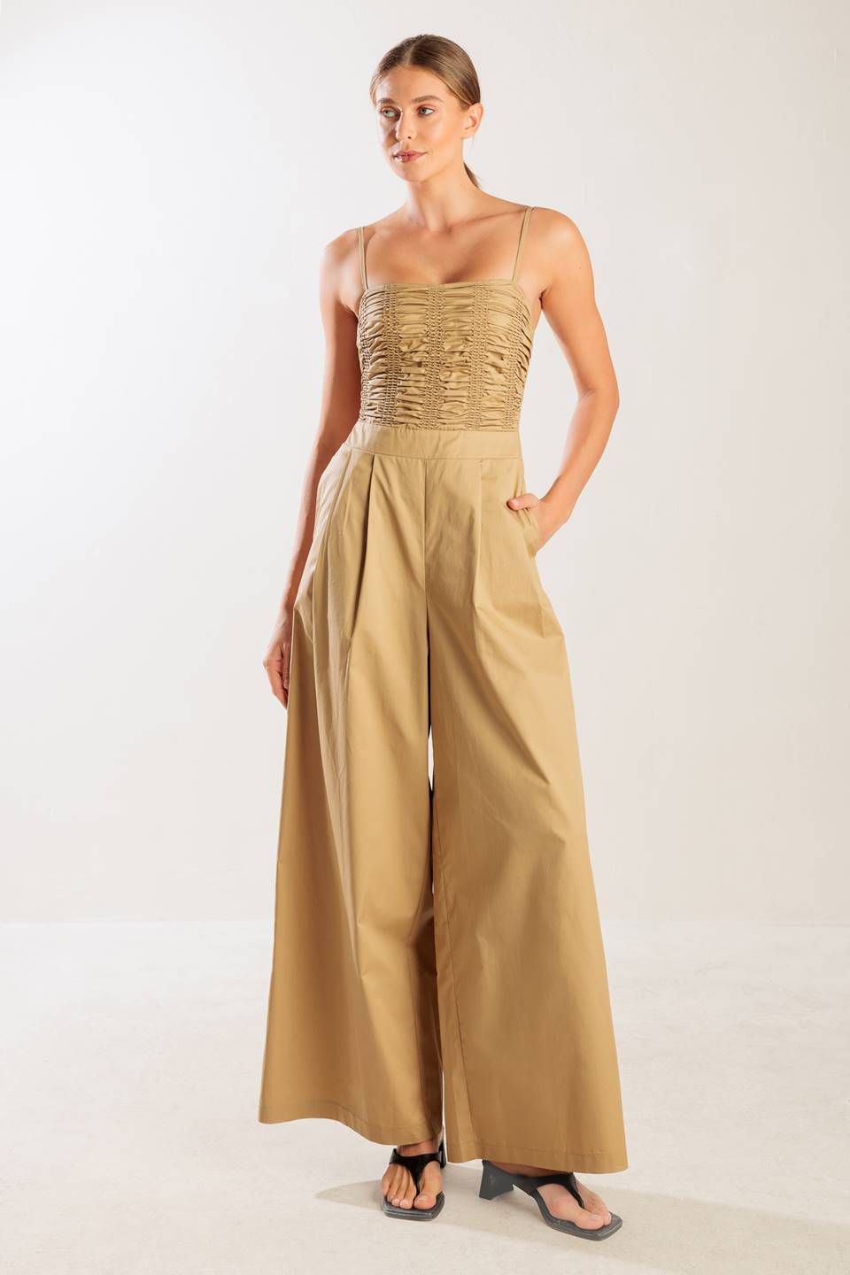 A solid woven jumpsuit featuring straight neckline, smocked bodice, straps, side pockets, wide leg, and back zipper closure