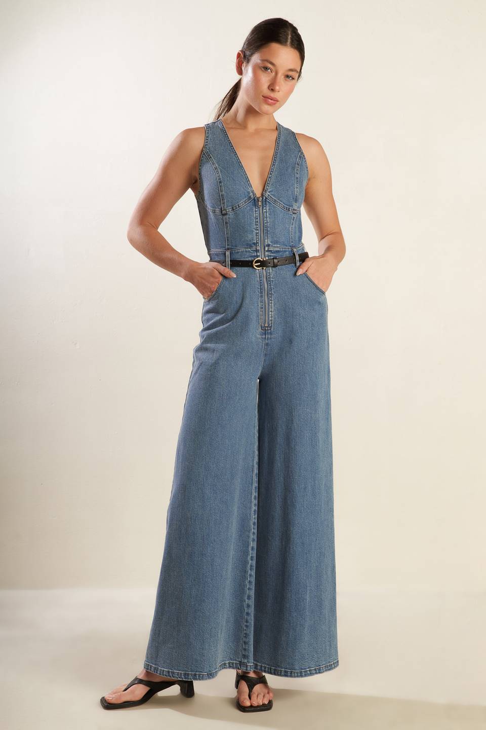 A washed denim jumpsuit featuring deep V neckline, sleeveless, front zipper closure, side pockets and wide leg.