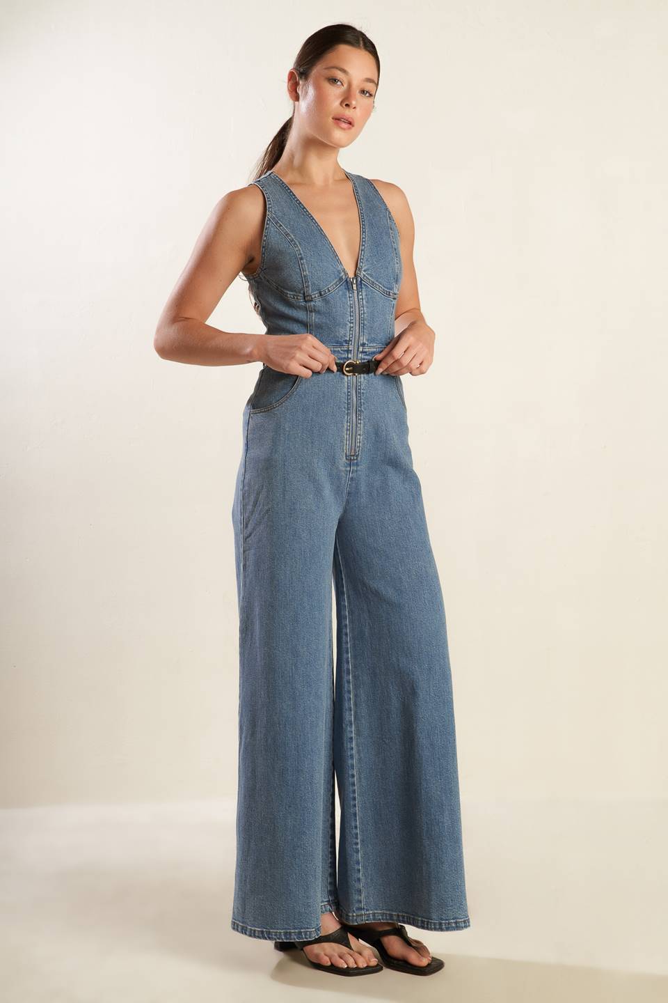 A washed denim jumpsuit featuring deep V neckline, sleeveless, front zipper closure, side pockets and wide leg.