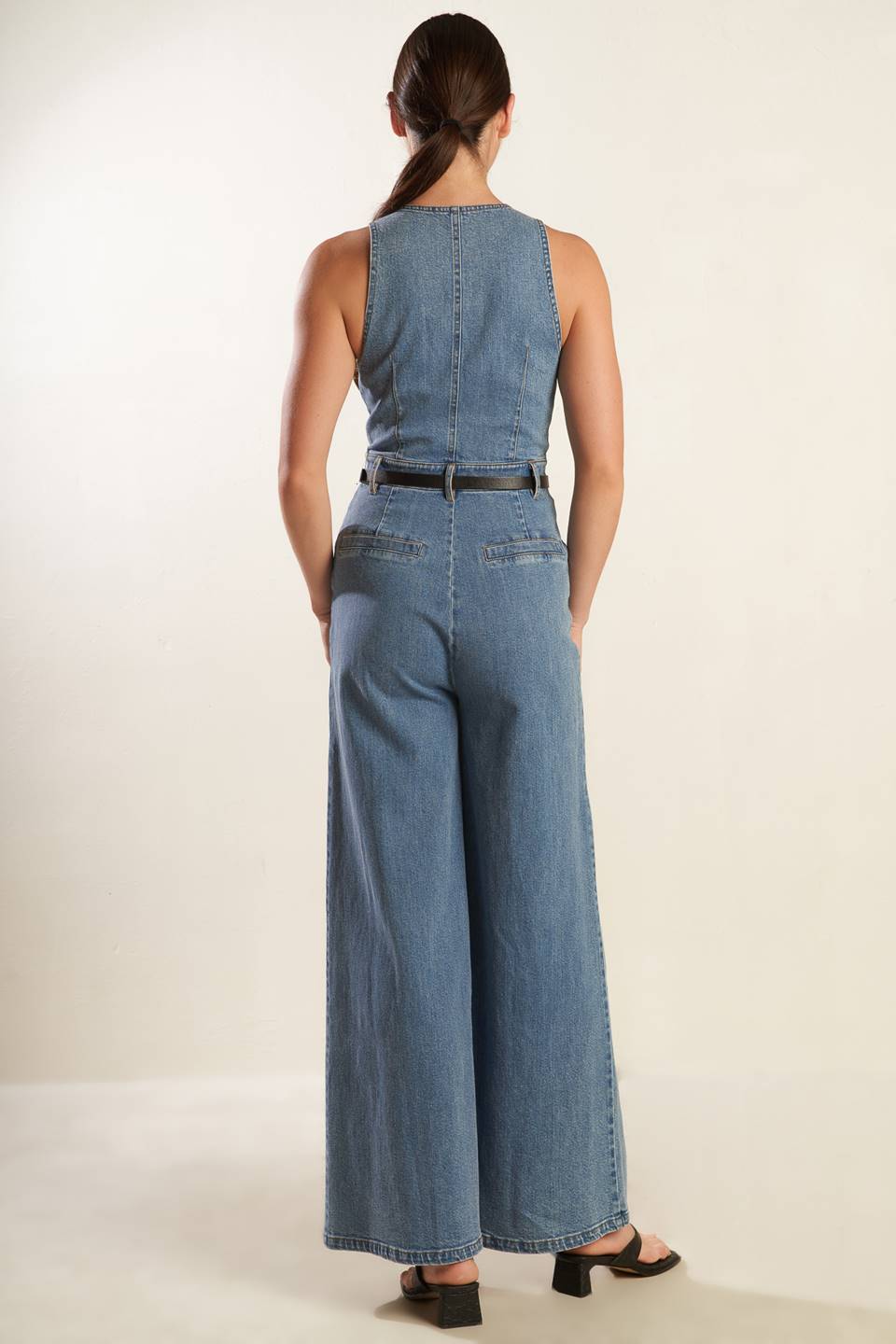 A washed denim jumpsuit featuring deep V neckline, sleeveless, front zipper closure, side pockets and wide leg.