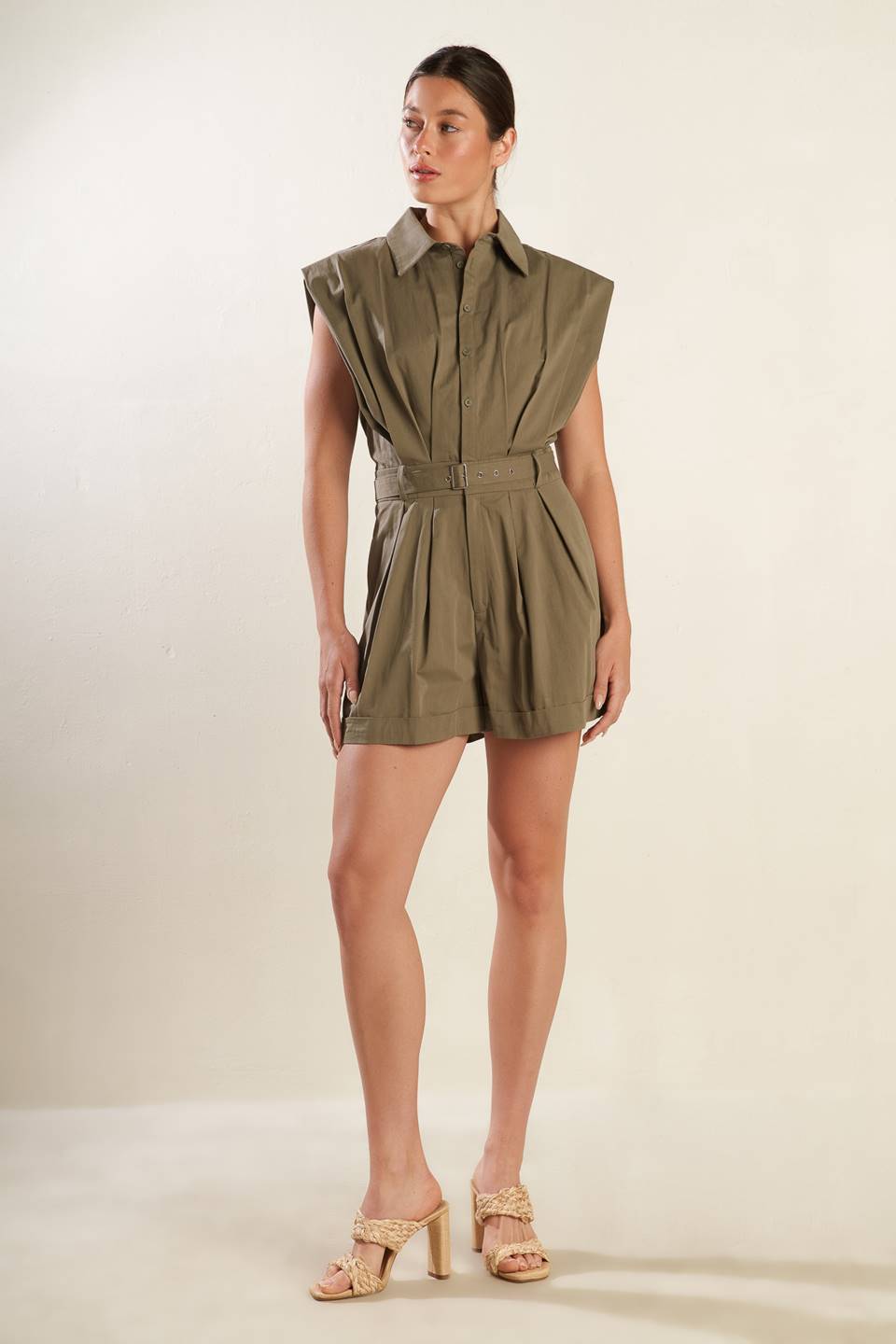 A solid olive woven romper featuring collar, oversize shoulder, front button down and zipper closure, self belt, side pockets and cuffed hemline.