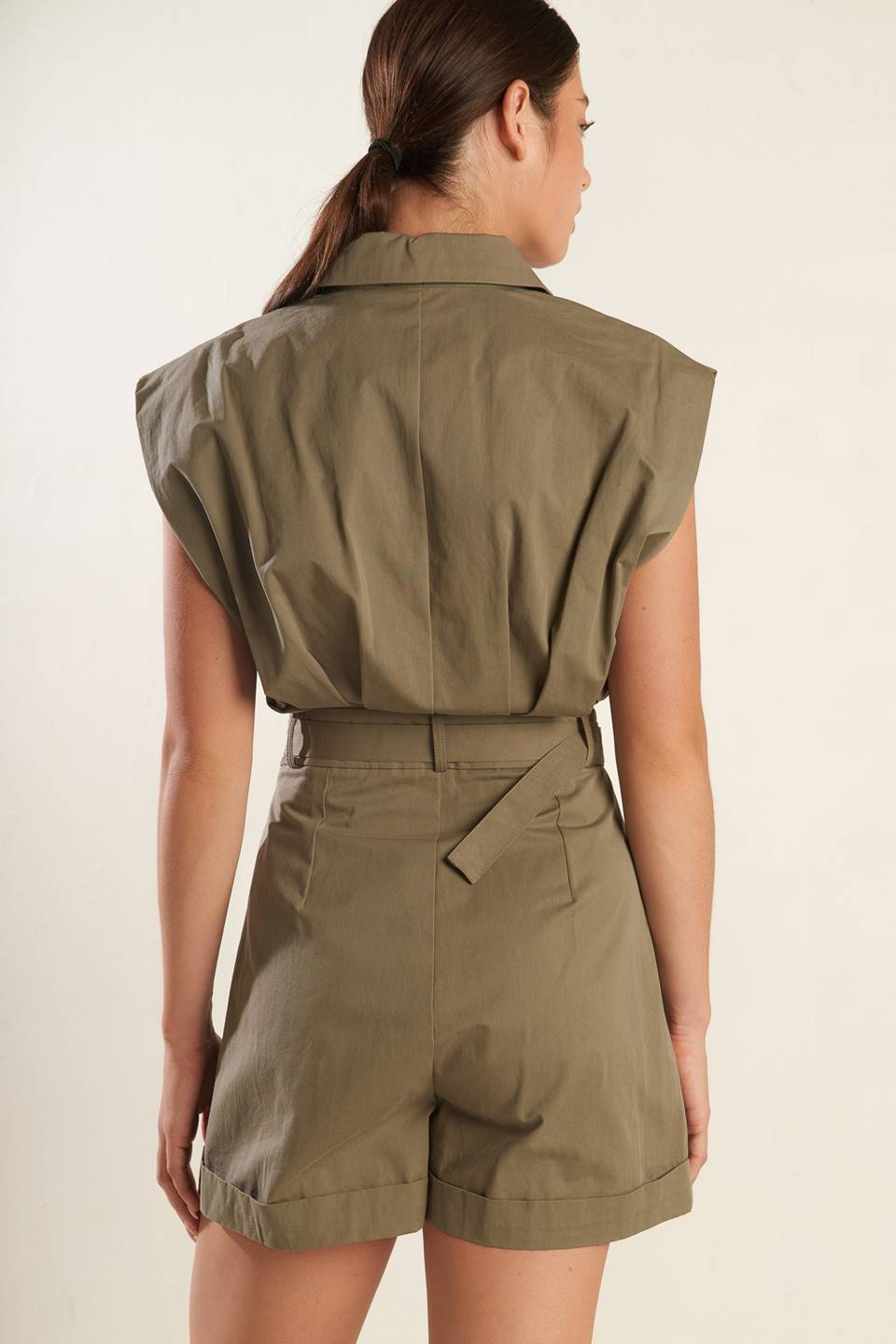 A solid olive woven romper featuring collar, oversize shoulder, front button down and zipper closure, self belt, side pockets and cuffed hemline.