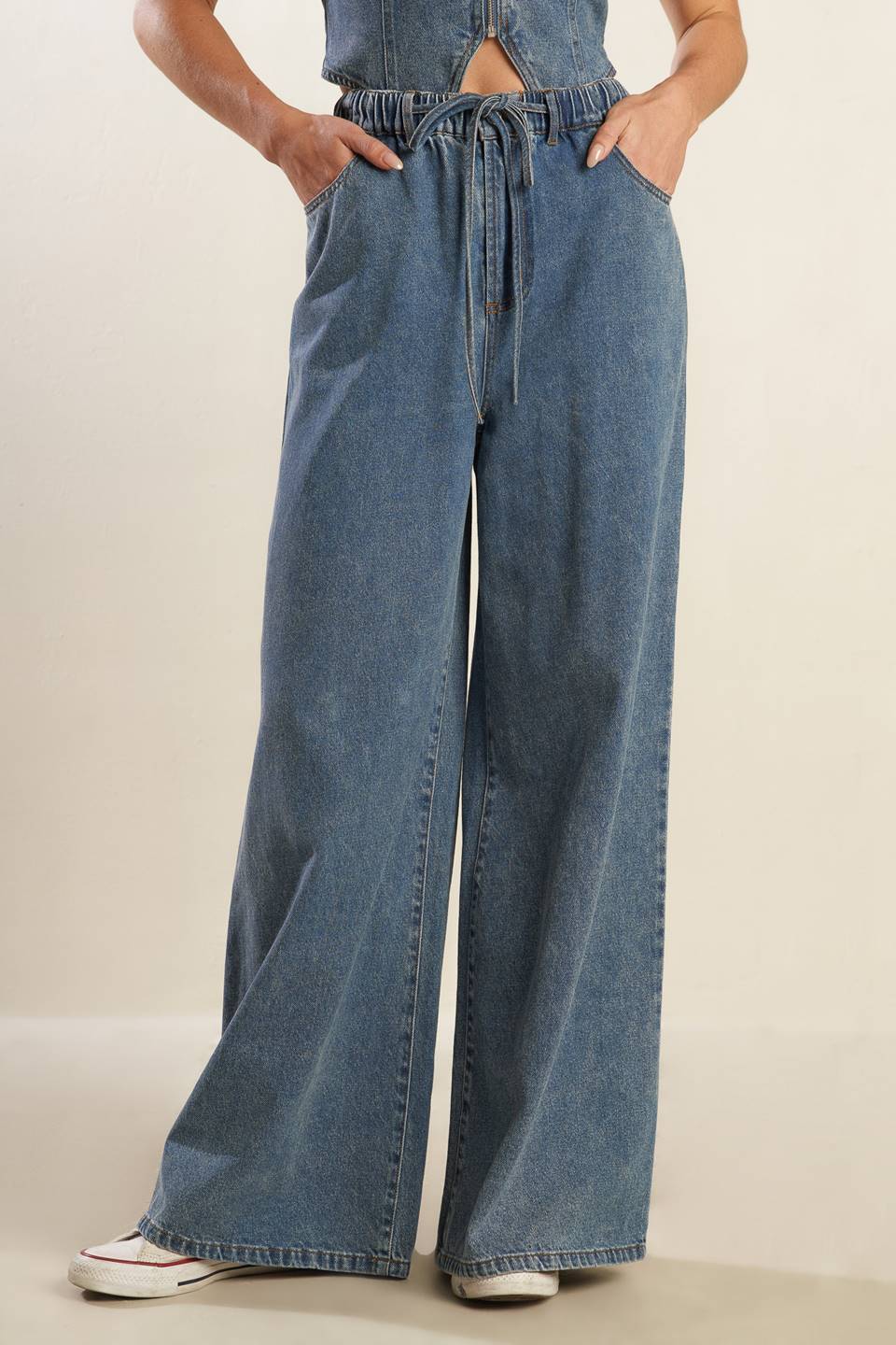 A washed denim pant featuring elasticized waistband with front tie, side pockets and wide leg.