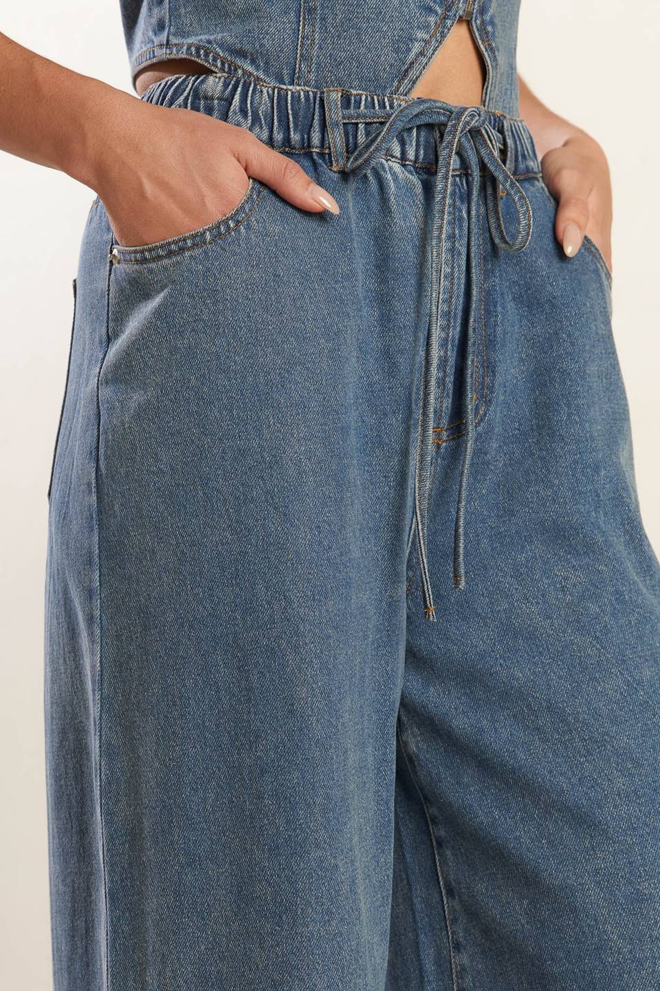 A washed denim pant featuring elasticized waistband with front tie, side pockets and wide leg.