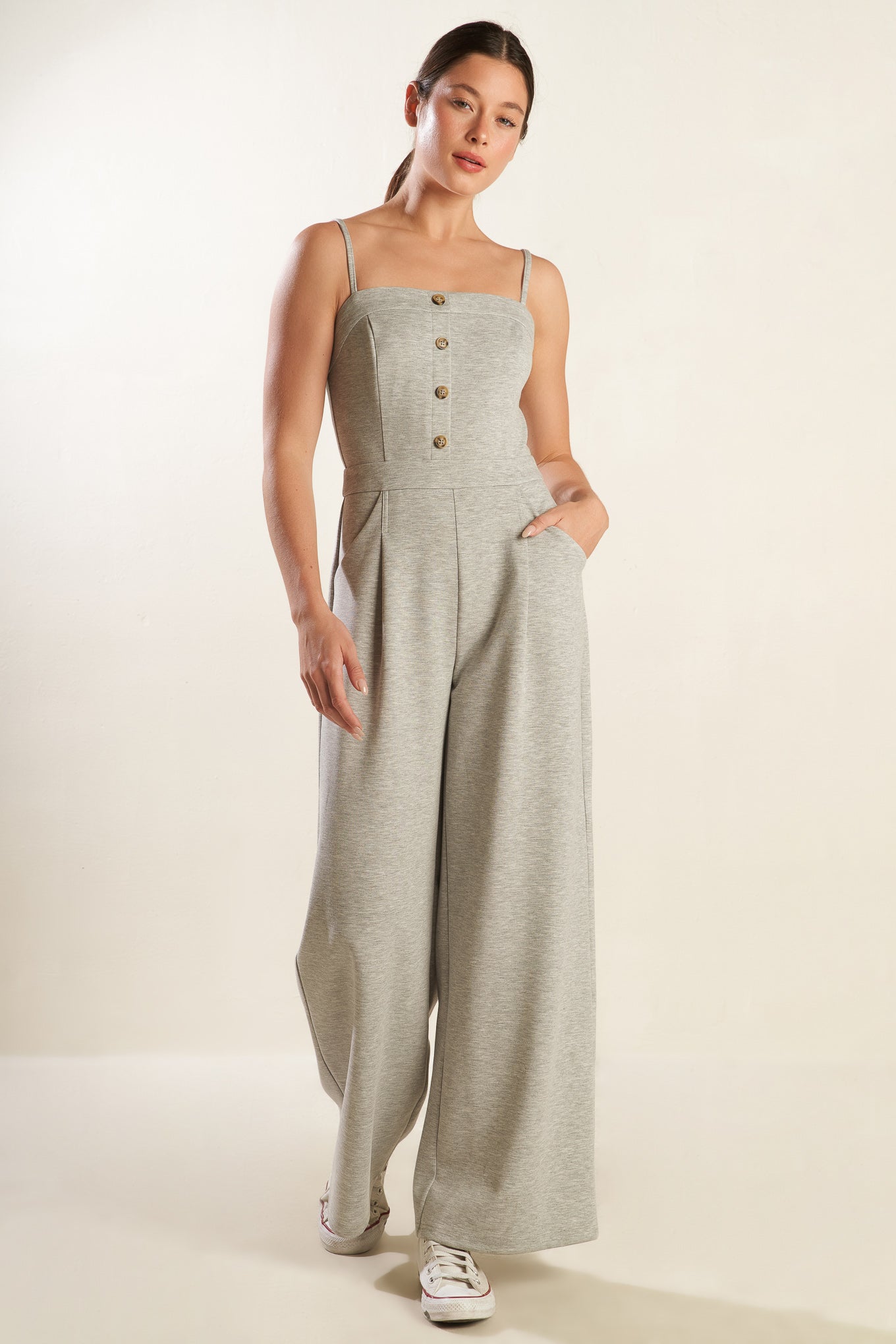 A solid heather grey knit jumpsuit featuring straight neckline with straps, button front detail, side pockets, wide leg and back zipper closure