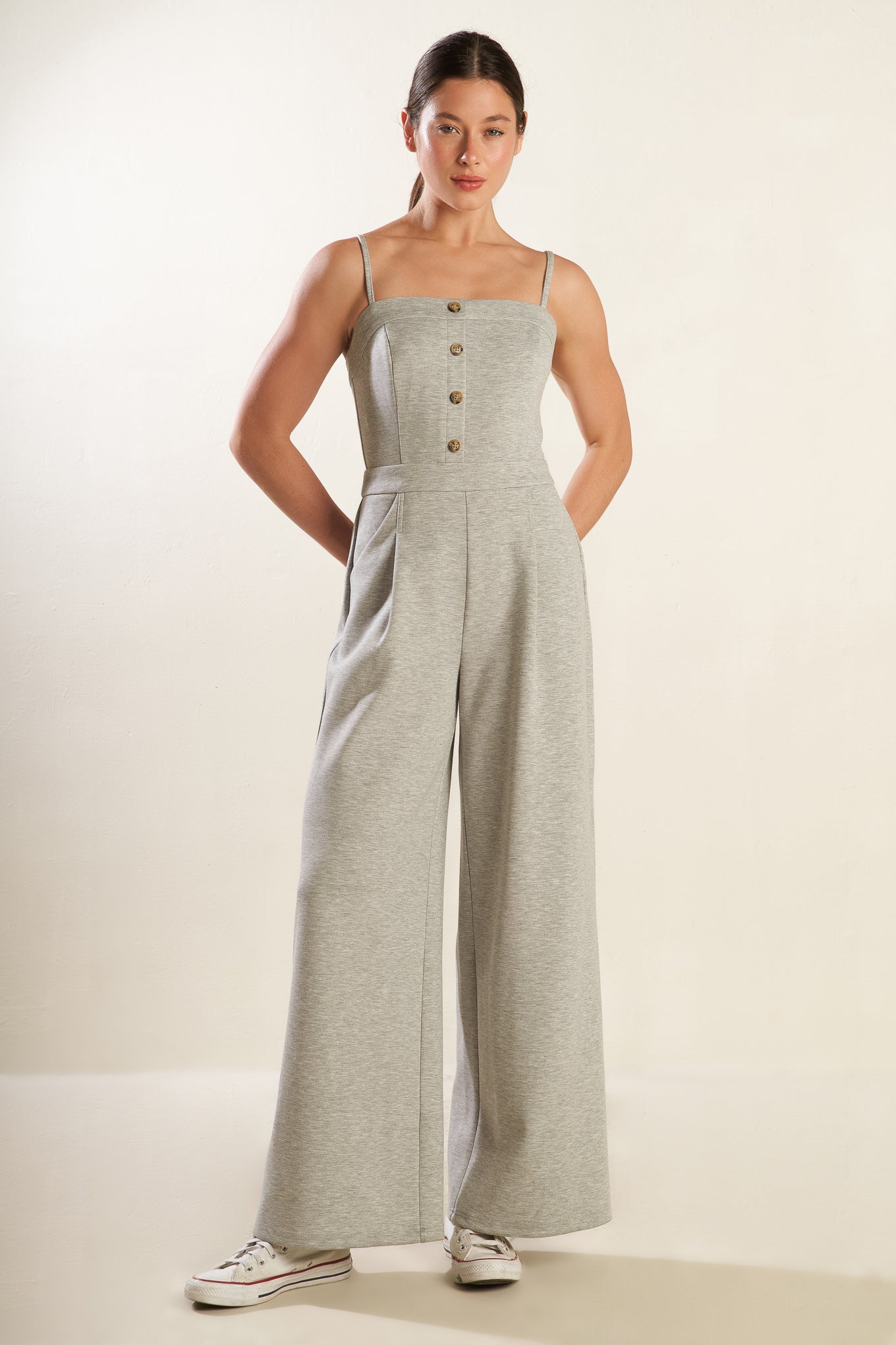 A solid heather grey knit jumpsuit featuring straight neckline with straps, button front detail, side pockets, wide leg and back zipper closure