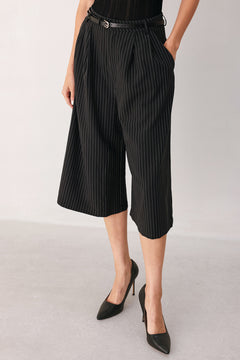 A woman wearing black cropped trousers with thin white vertical pinstripes, featuring a matching black belt with a silver buckle | FREEMARKET