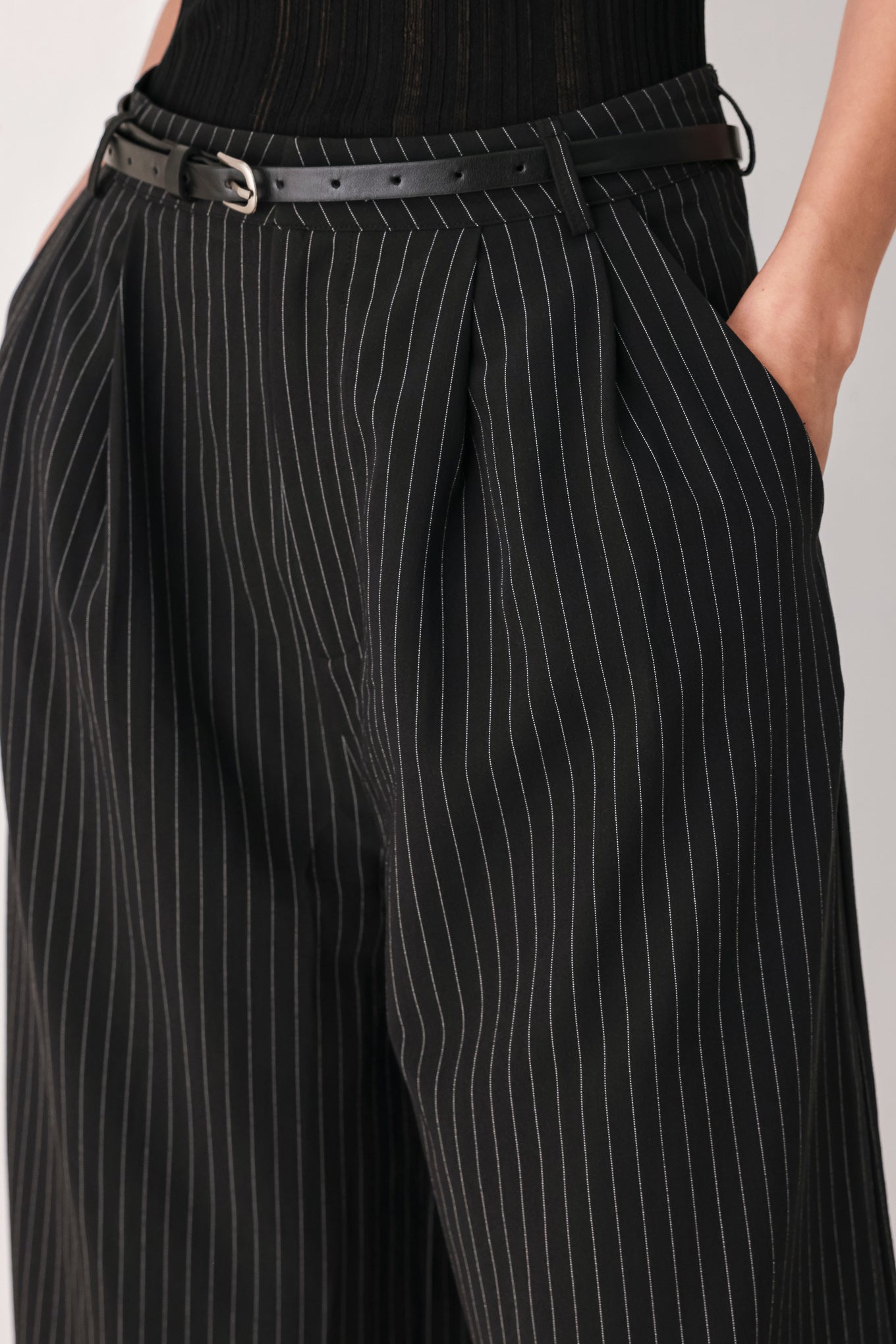 A woman wearing black cropped trousers with thin white vertical pinstripes, featuring a matching black belt with a silver buckle | FREEMARKET