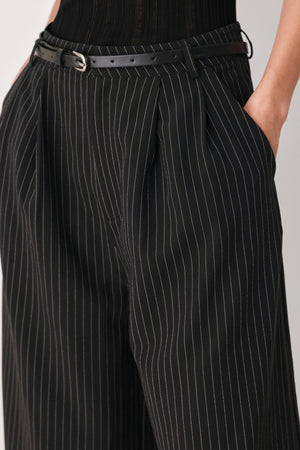 A woman wearing black cropped trousers with thin white vertical pinstripes, featuring a matching black belt with a silver buckle | FREEMARKET