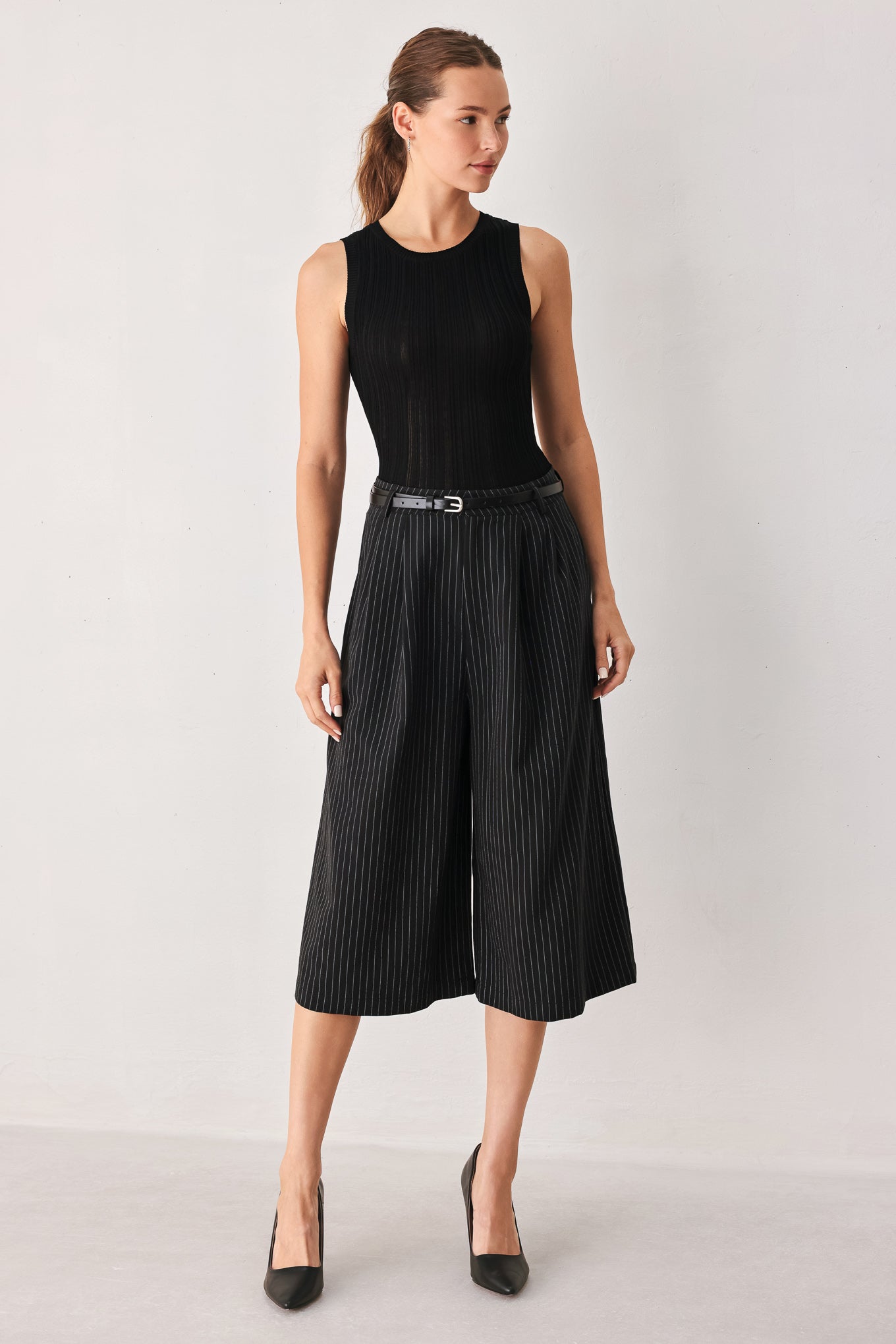 A woman wearing black cropped trousers with thin white vertical pinstripes, featuring a matching black belt with a silver buckle | FREEMARKET