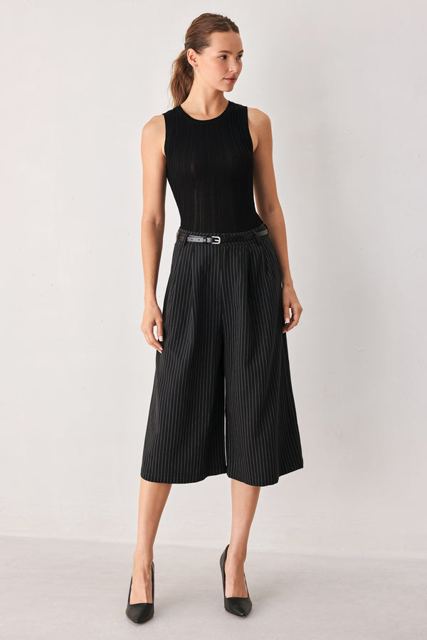 A woman wearing black cropped trousers with thin white vertical pinstripes, featuring a matching black belt with a silver buckle | FREEMARKET