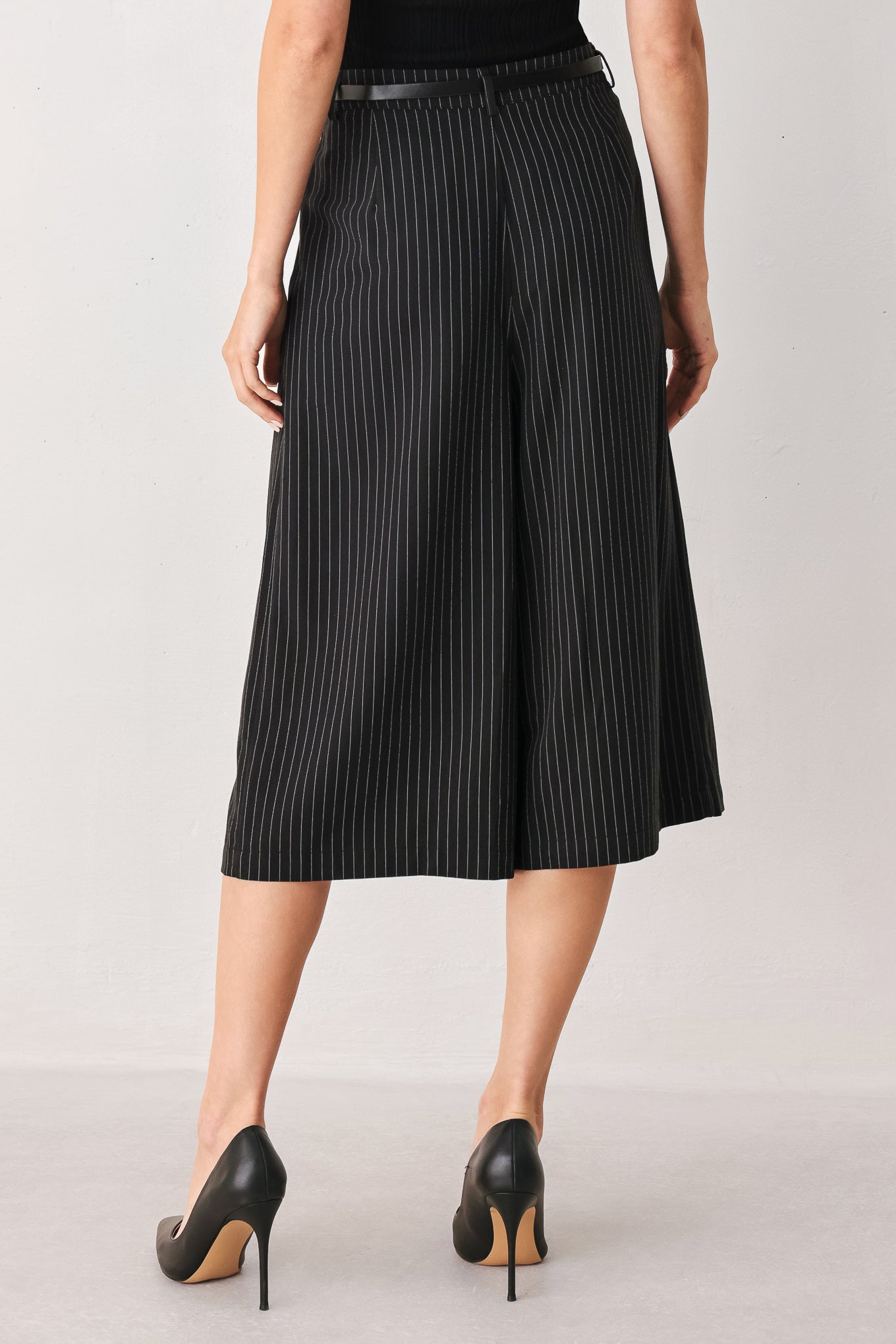 A woman wearing black cropped trousers with thin white vertical pinstripes, featuring a matching black belt with a silver buckle | FREEMARKET
