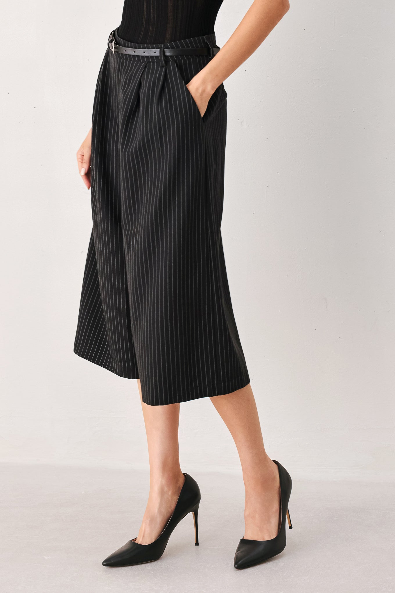 A woman wearing black cropped trousers with thin white vertical pinstripes, featuring a matching black belt with a silver buckle | FREEMARKET
