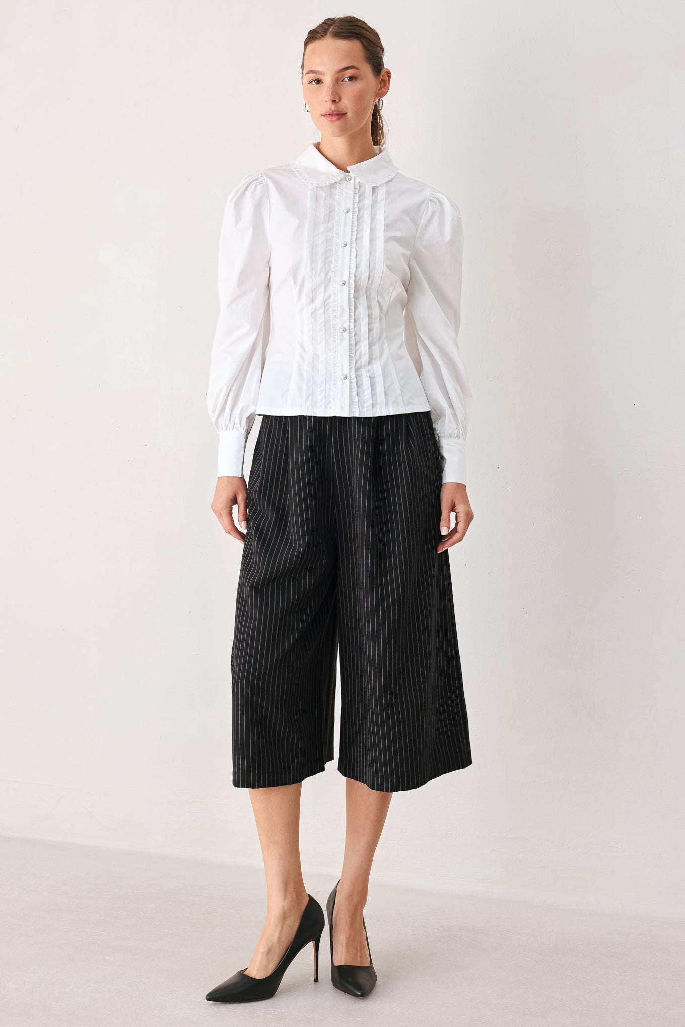 A woman wearing black cropped trousers with thin white vertical pinstripes, featuring a matching black belt with a silver buckle | FREEMARKET