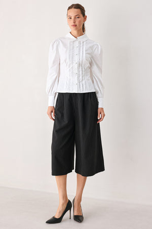 A woman wearing black cropped trousers with thin white vertical pinstripes, featuring a matching black belt with a silver buckle | FREEMARKET